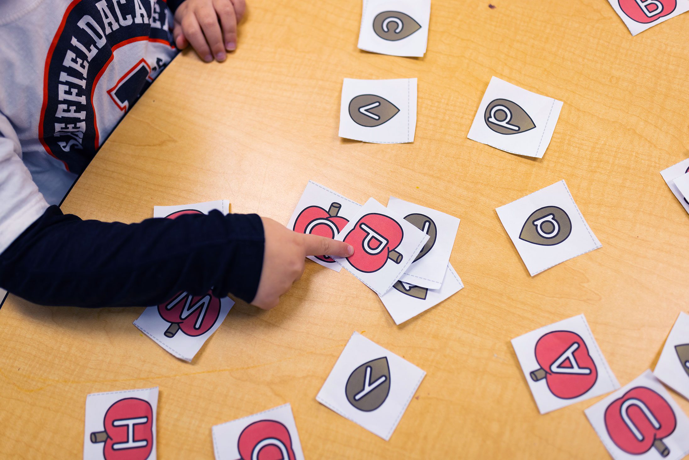 Student pointing to a letter card during a phonics activity.