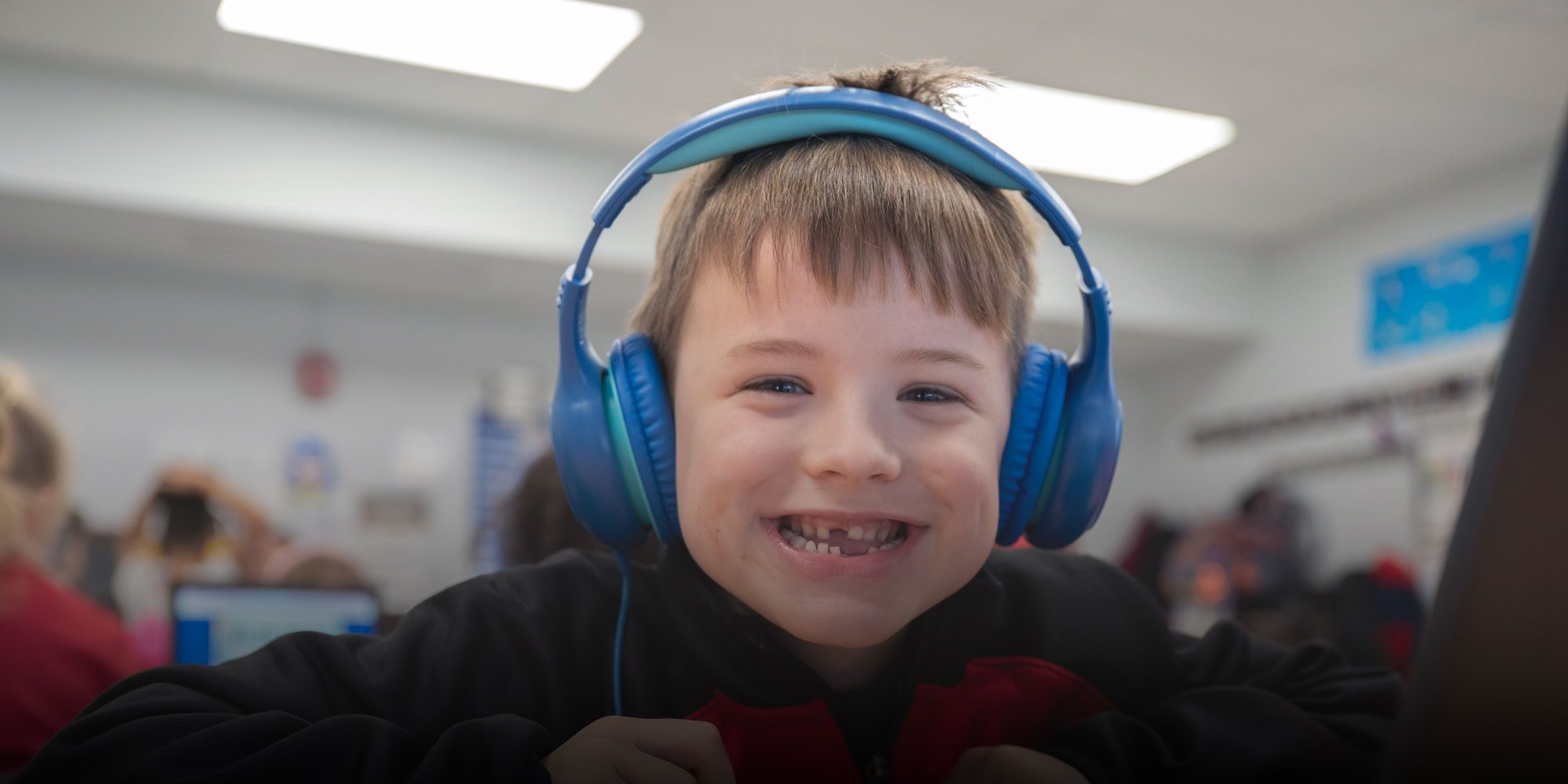Smiling student wearing blue headphones in a classroom.